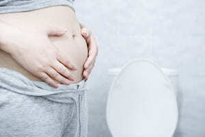A person standing next to the toilet with their hands over their bloated belly