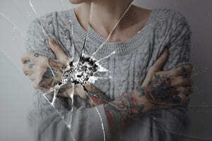 Woman standing in front of a broken mirror reflecting her wounded feelings
